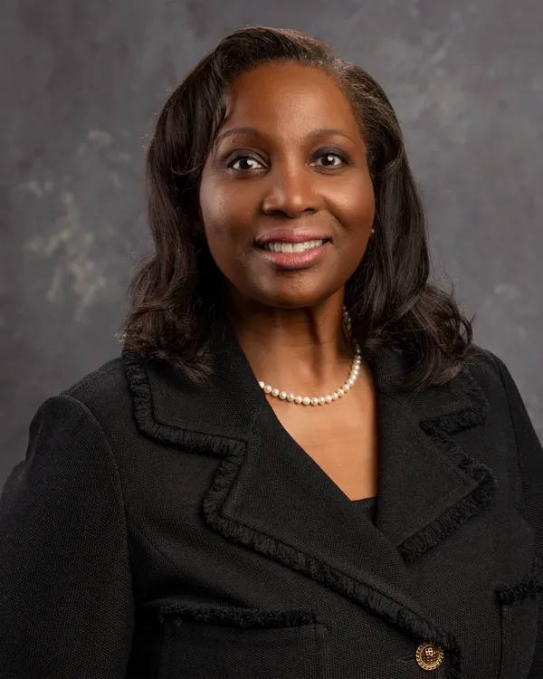 Official portrait of Federal Reserve Governor Lisa D. Cook seated in a dark blazer with the American flag behind her.